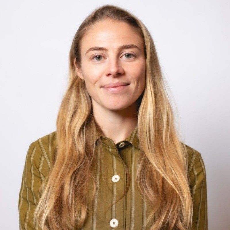 Woman with long blonde hair wearing a striped olive green shirt smiling against a plain white background.